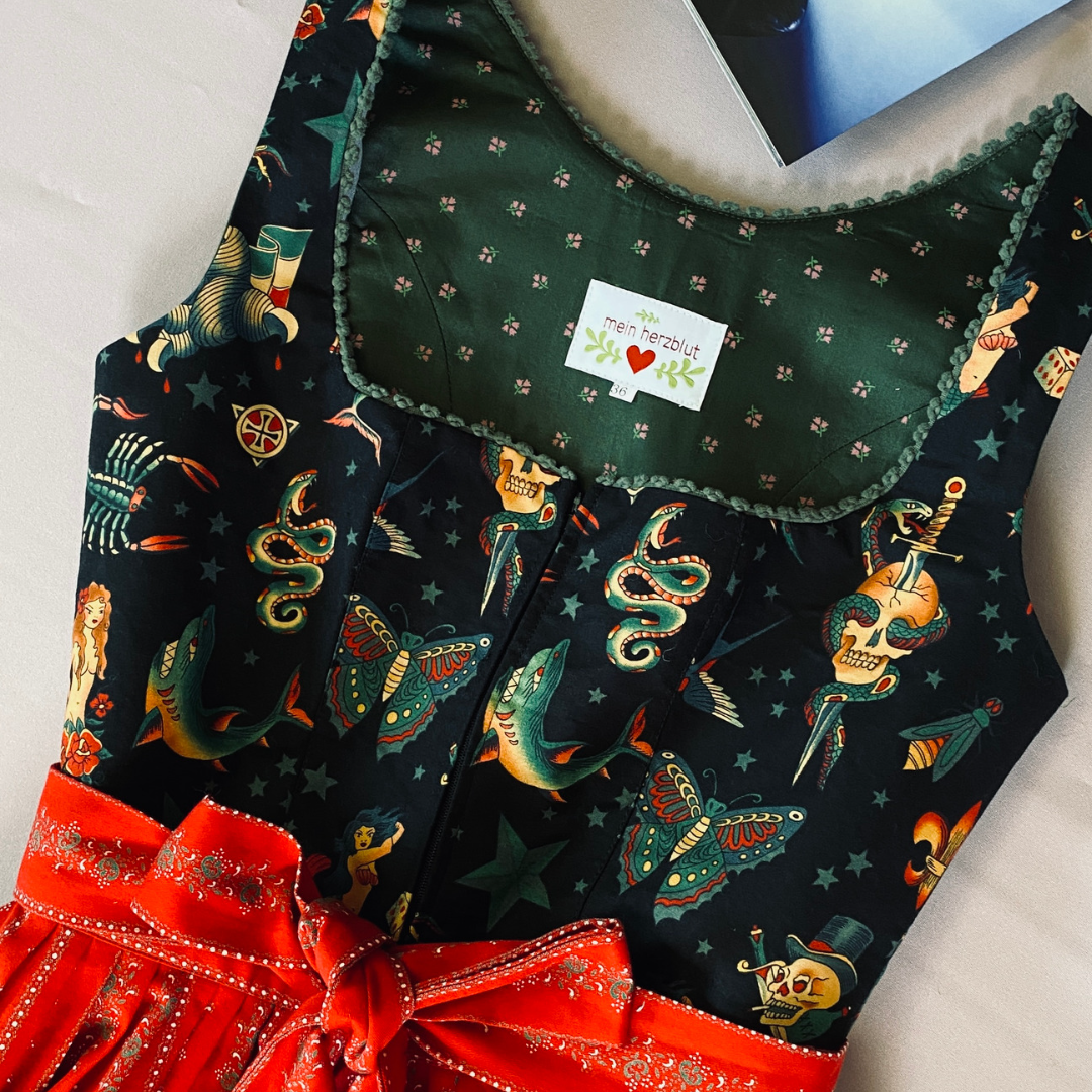 Das besondere Design des Dirndls verbindet die zeitlose Schönheit der Tracht mit modernen Trends. Die schwarzen Tattoo-Motive auf dem Dirndl sind ein einzigartiges und kreatives Detail, das das traditionelle Outfit aufpeppt