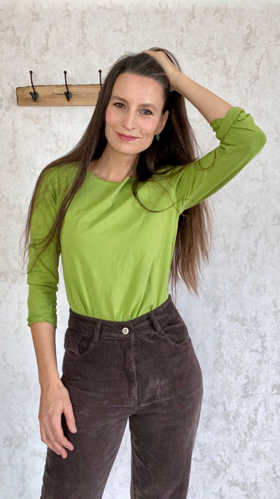 A woman wearing a retro green top and brown Cordhose retro 1990 pants made of Baumwolle from Italy.