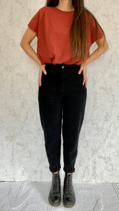 A woman wearing a red top and black Cordhose retro 1990 pants made by made in Italy.