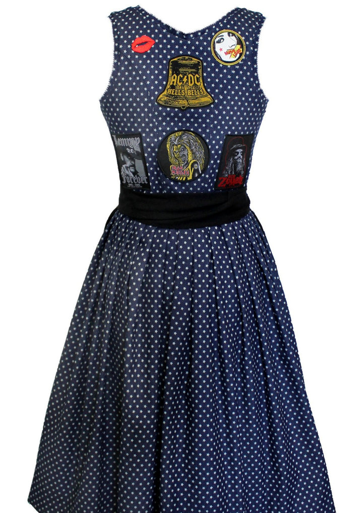 Hier siehtst Du das Jeans Rocker Dirndl von hinten. Man sieht hier genau wie es gemacht wurde. Das komplette Dirndl ist dunkelblau indigo bedruckt mit helleren Sternen. Die Aufnäher wurde auf der Rückseite aufgenäht. Eine große Glocke von ACDC darunter Iron Maiden. Links davon Lemmy und rechts Rob Zombie. Oben an den Schulterblättern sind no name Aufnäher aufgenäht. Einer davon ist ein Kussmund in rot. Die Farben harmonieren super zusammen. 